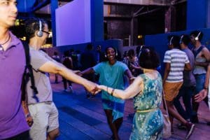 Game participants wander and wonder as they listen to Janani’s instructions and musings. They look up to the sky, hold hands, dance, and laugh together.