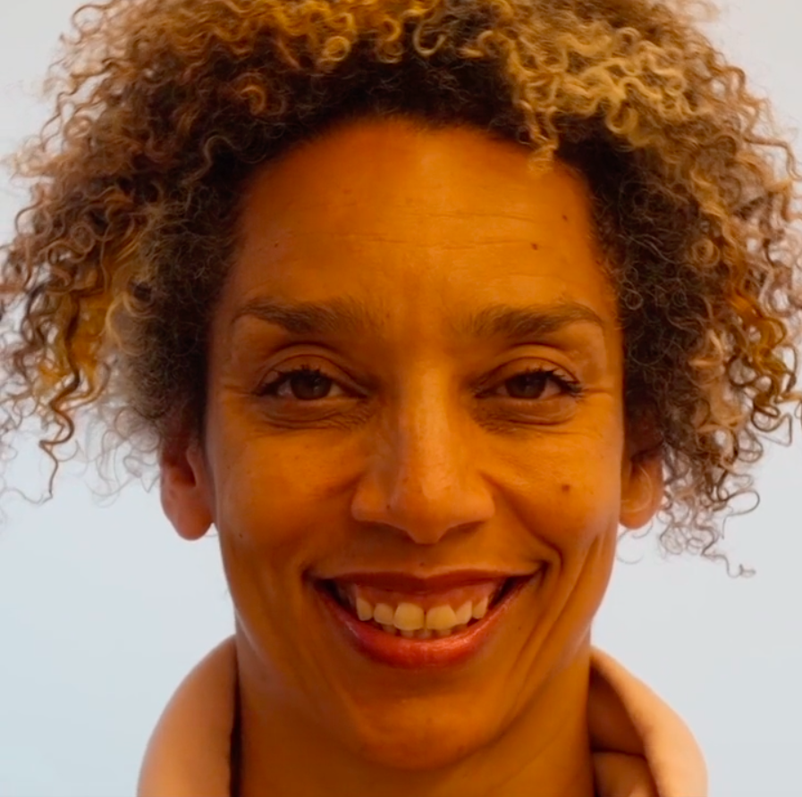 Alice Sheppard, a light skinned multiracial Black woman with brown eyes and blonde, mustard, and brown striped curly hair, wears a peach colored sweatshirt. In this video, she performs a face dance moving in and out of a series of intense facial expressions to create a dance capturing some of the feelings of forgetting. In between some of these expressions, an AI intervenes. Time slows as we watch the AI create the transition, by changing Alice’s facial features and interpreting her face through its own lens. In this still, she smiles.