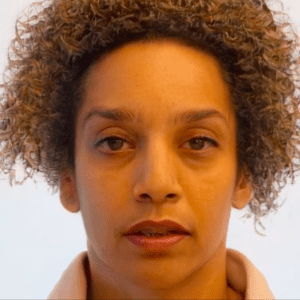 Alice Sheppard, a light skinned multiracial Black woman with brown eyes and blonde, mustard, and brown striped curly hair, wears a peach colored sweatshirt. In this video, she performs a face dance moving in and out of a series of intense facial expressions to create a dance capturing some of the feelings of forgetting. In between some of these expressions, an AI intervenes. Time slows as we watch the AI create the transition, by changing Alice’s facial features and interpreting her face through its own lens. AI has smoothed her skin and blurred her eyes. Her both is slightly open. Neutral expression.