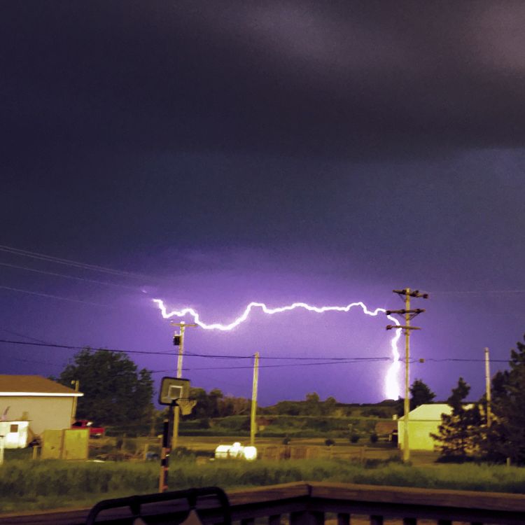 bolt of lightning against telephone poles with a purple sky